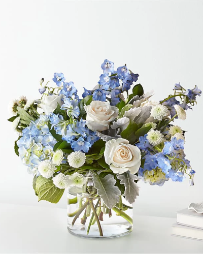 <p>This soothing bouquet features pale blue flowers—such as hydrangea or delphinium—paired with crisp white roses and a lush mix of greenery. Arranged in a simple clear glass vase, the design highlights the natural elegance of each bloom while maintaining a clean, modern feel.</p>