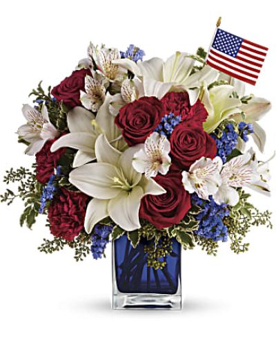 <p>Thisbouquet features red roses, red carnations, white Asiatic lilies, white alstroemeria, and blue statice. Accented with green pitta negra and seeded eucalyptus, the blooms are arranged in a cobalt blue glass cube and accompanied by a small American flag for a patriotic touch.</p>