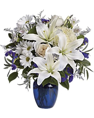 <p>This design features a stunning mix of blue hydrangea, creamy roses, white lilies, white alstroemeria, and a blend of yellow and white chrysanthemums. All blooms are beautifully arranged in a striking blue glass vase that enhances the soft and serene color palette, creating a harmonious and inviting display.</p>